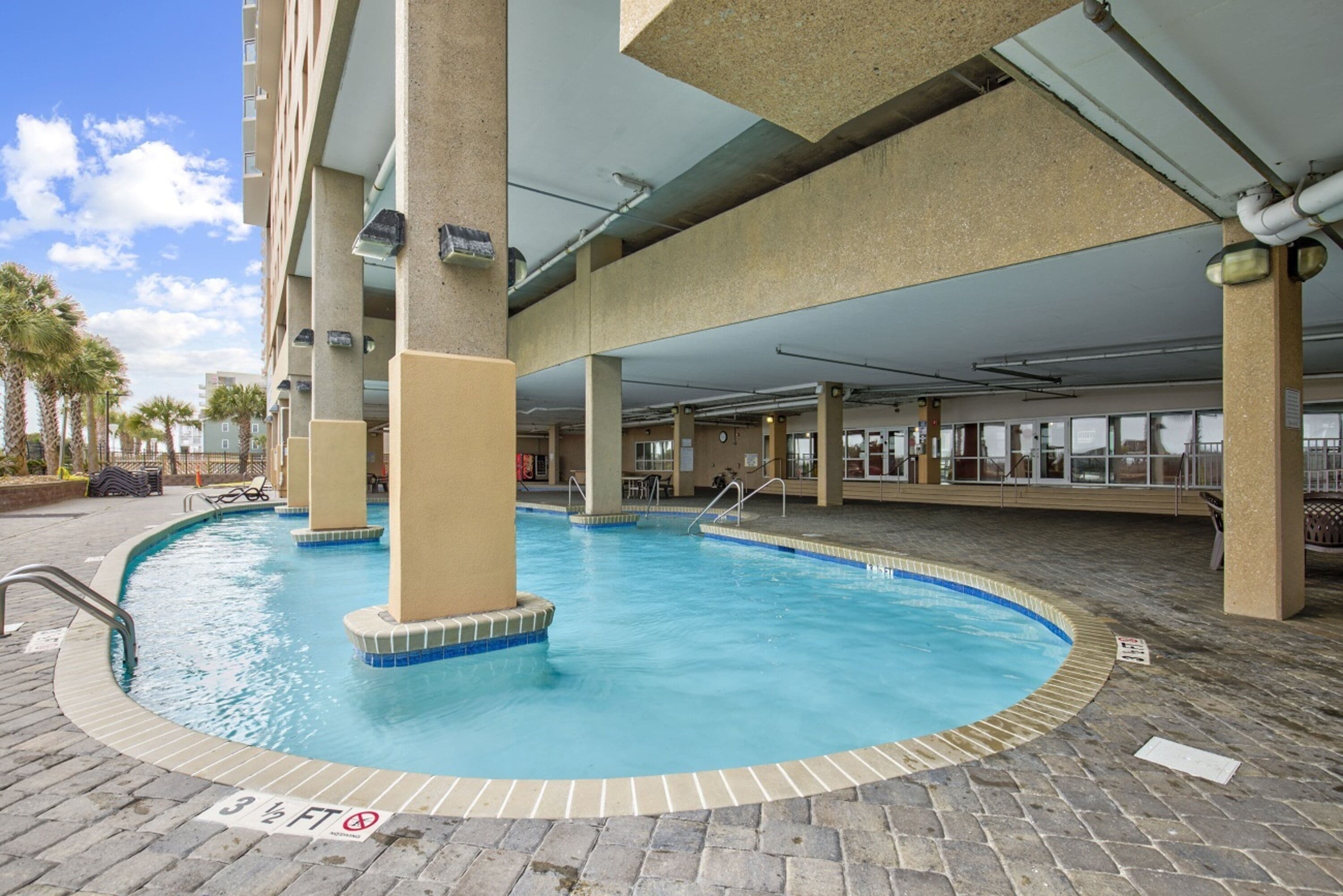 An indoor swimming pool with a tiled edge, surrounded by a brick floor and supported by concrete pillars.