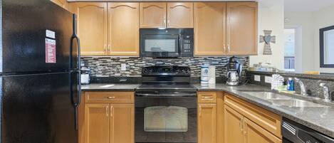 A kitchen with wooden cabinets, a black refrigerator, a microwave, an oven, and a dishwasher.