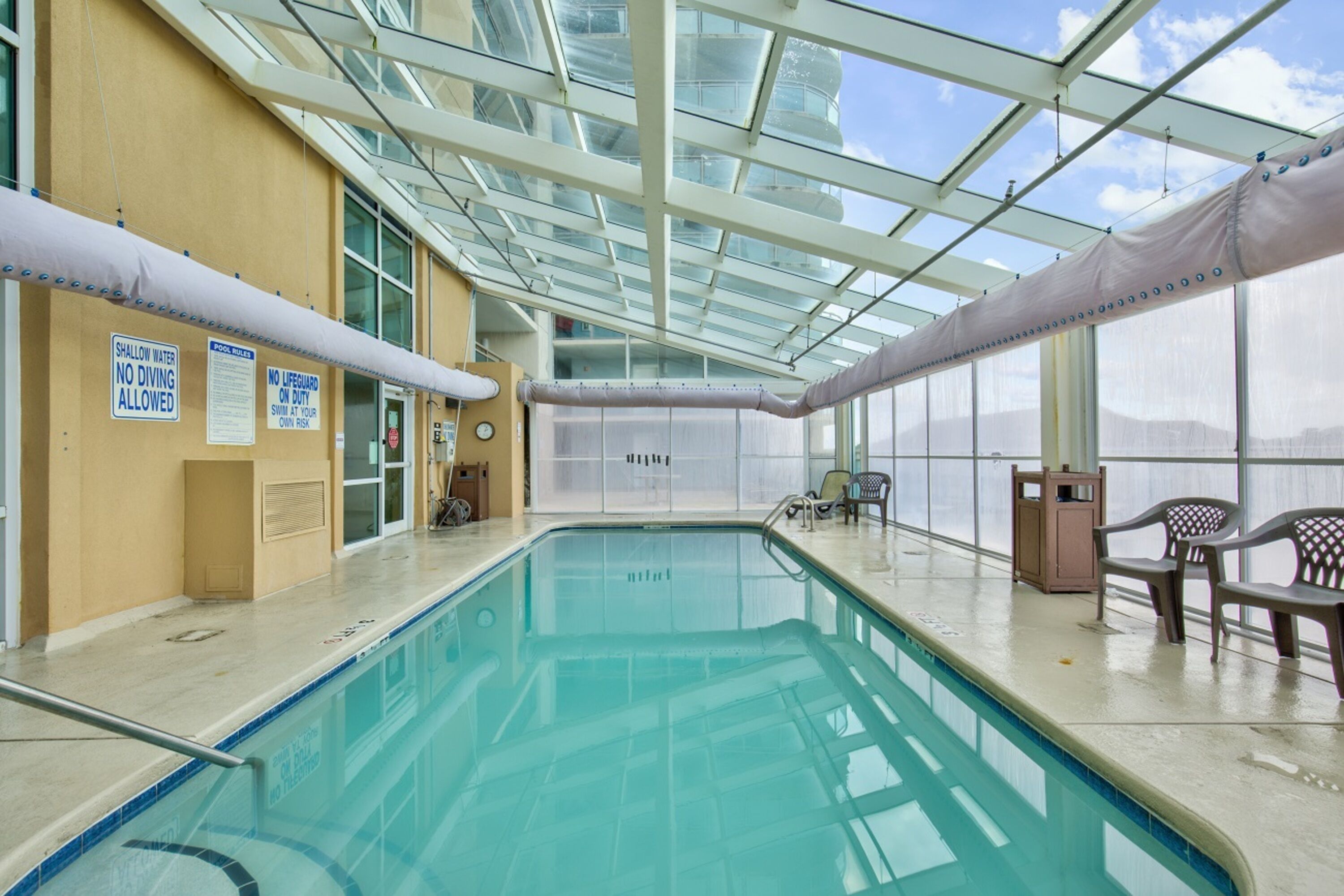 An indoor swimming pool with clear signage, a glass ceiling, and seating areas.