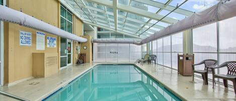 An indoor swimming pool with clear signage, a glass ceiling, and seating areas.
