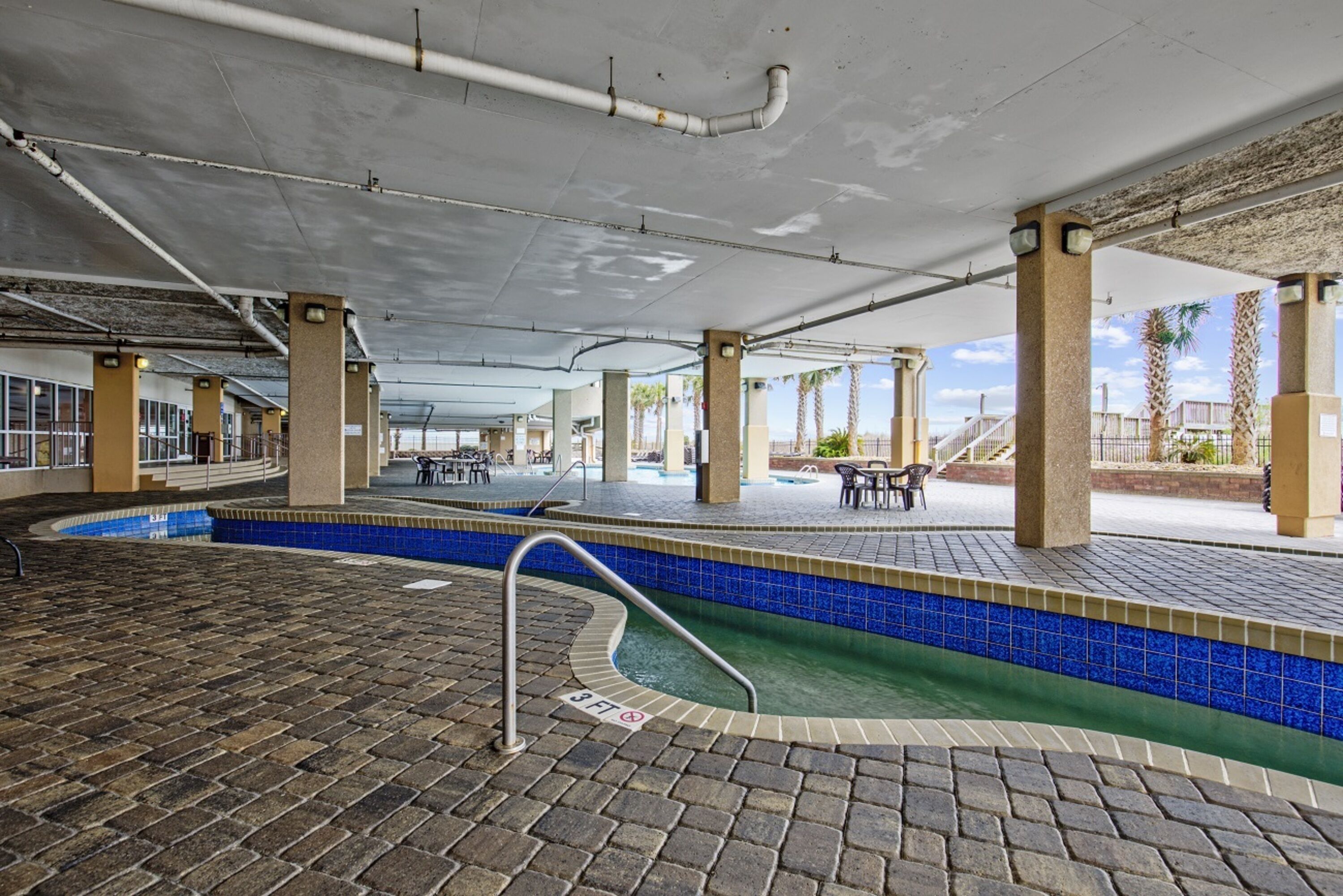 An indoor swimming pool with a tiled edge, a brick floor, and a ceiling with visible pipes.