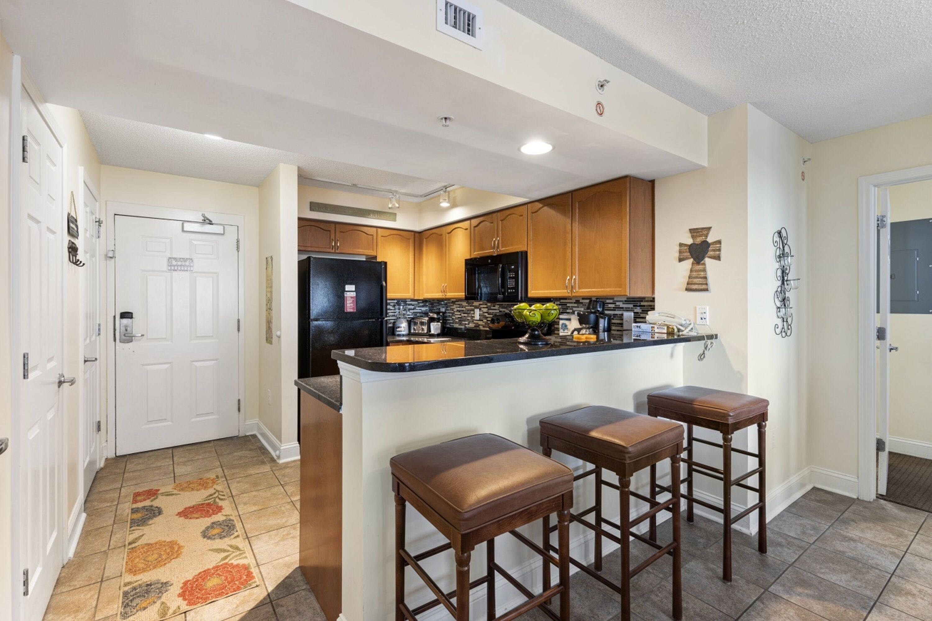 A modern kitchen with wooden cabinets, a black refrigerator, a microwave, and a bar area with stools.