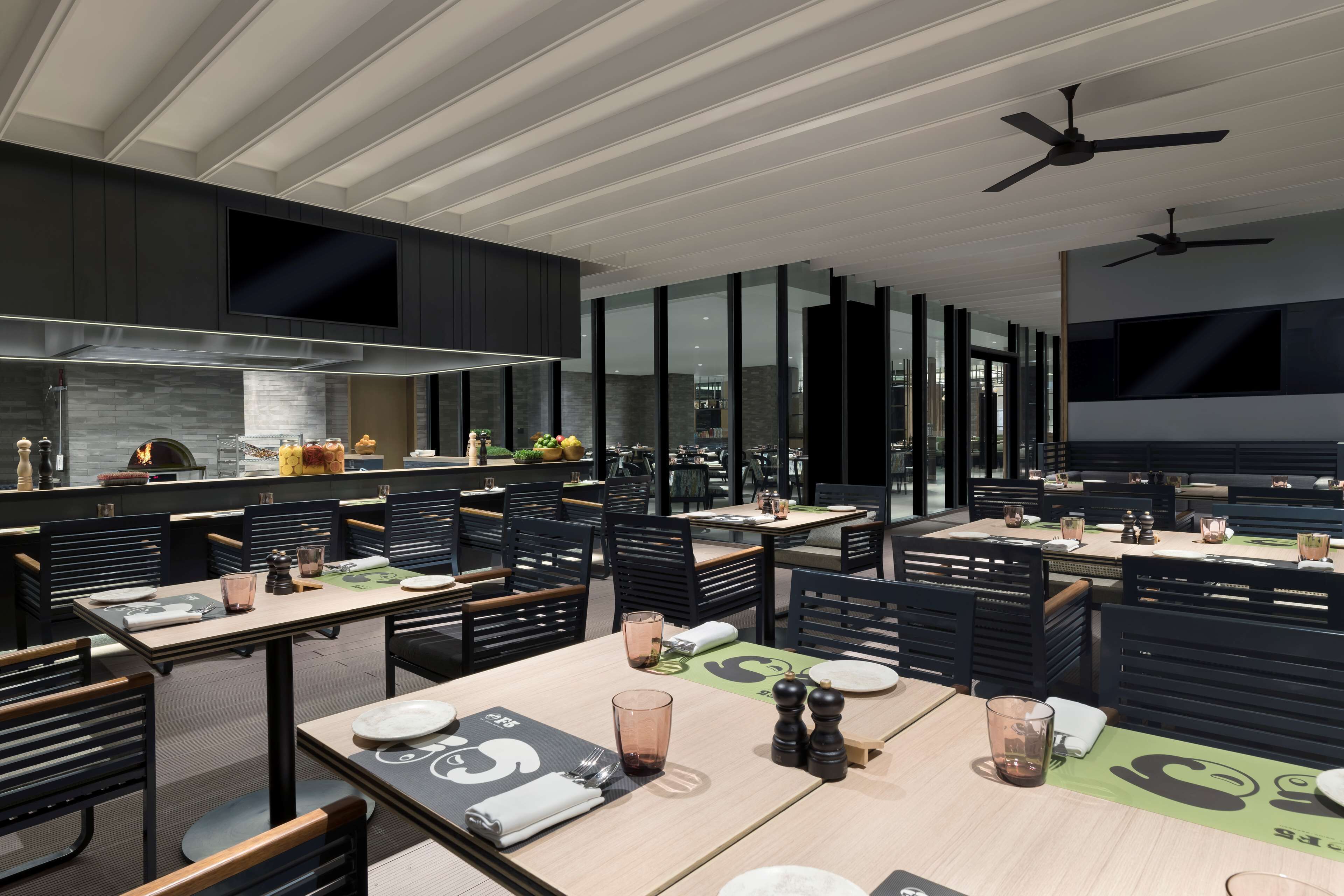A modern restaurant with multiple dining tables, black chairs, and ceiling fans.