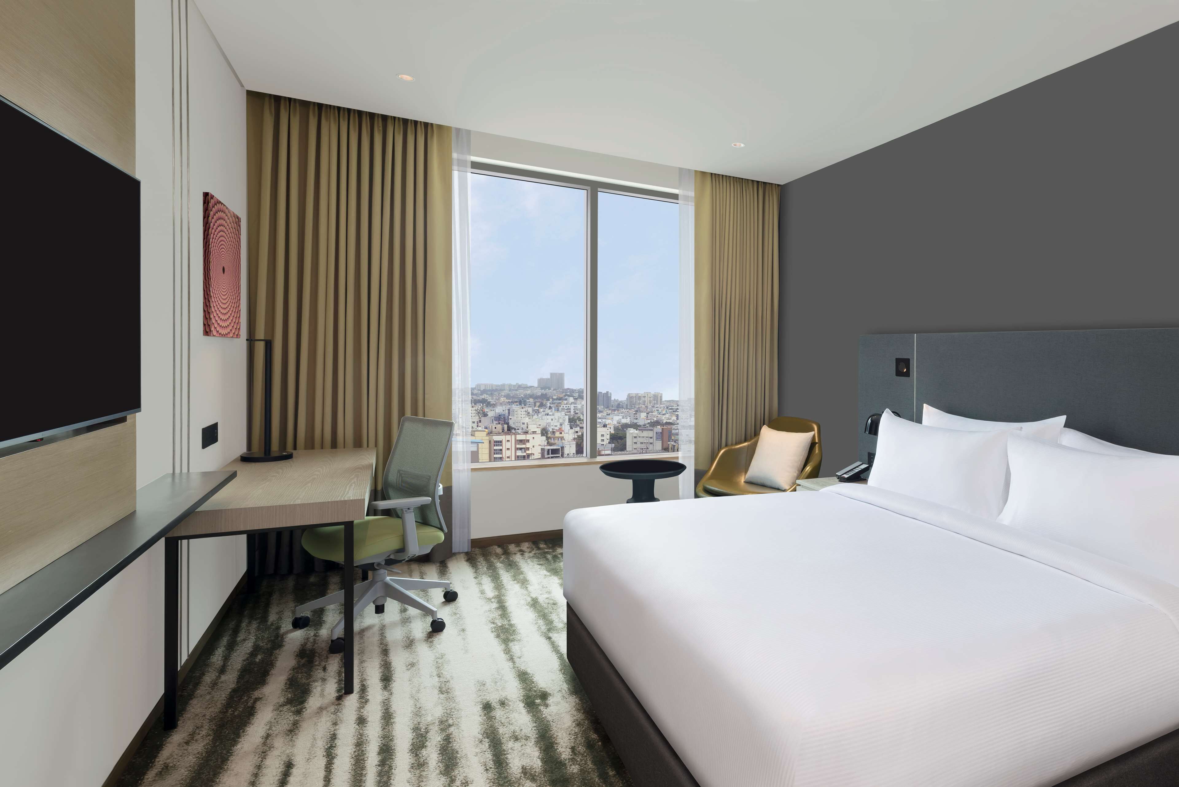 Une chambre d’hôtel avec un grand lit, un bureau, une chaise et une vue sur la ville grâce à une grande fenêtre.