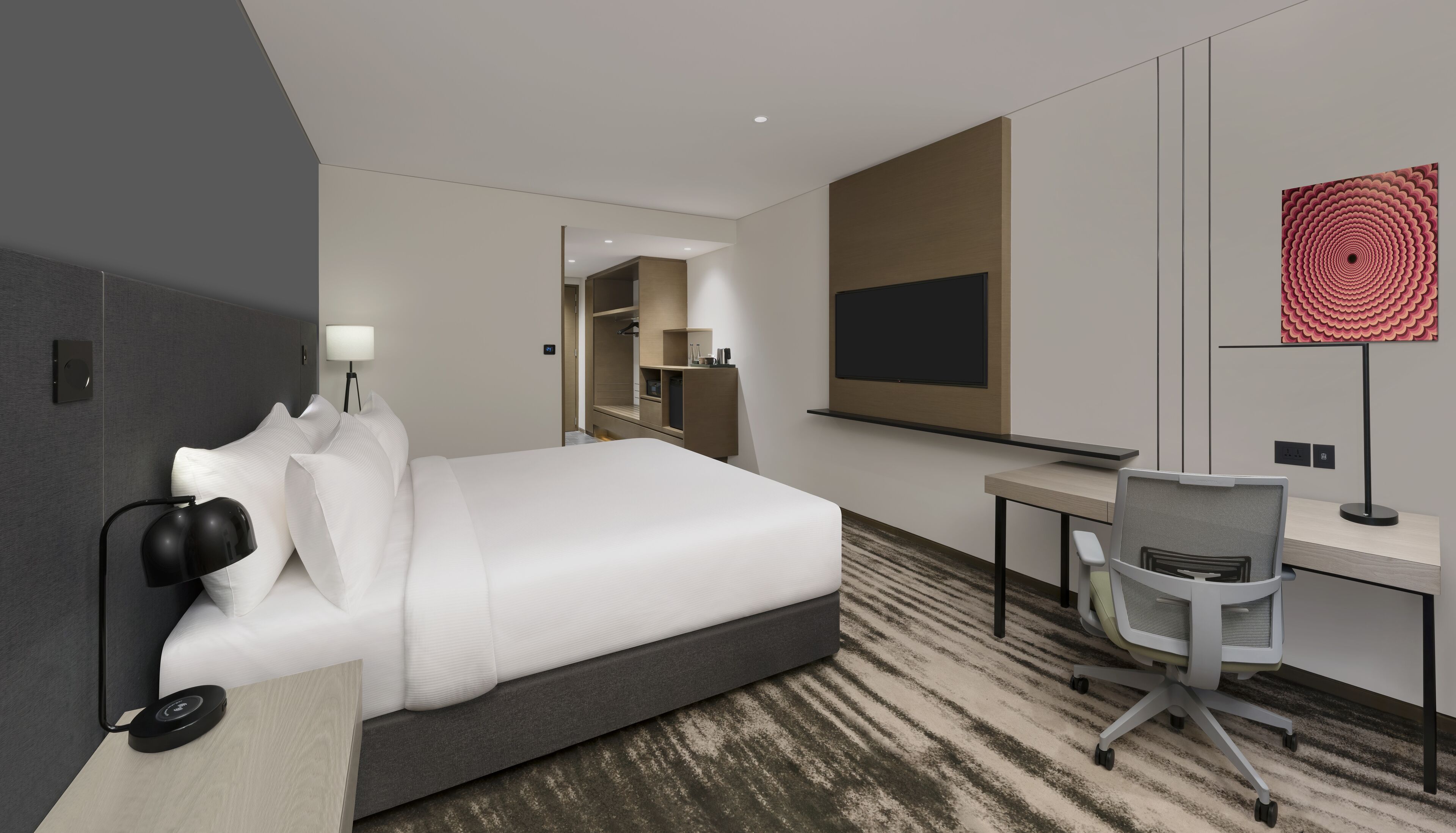A modern hotel room with a large bed, a desk, a chair, a TV, and a unique artwork on the wall.