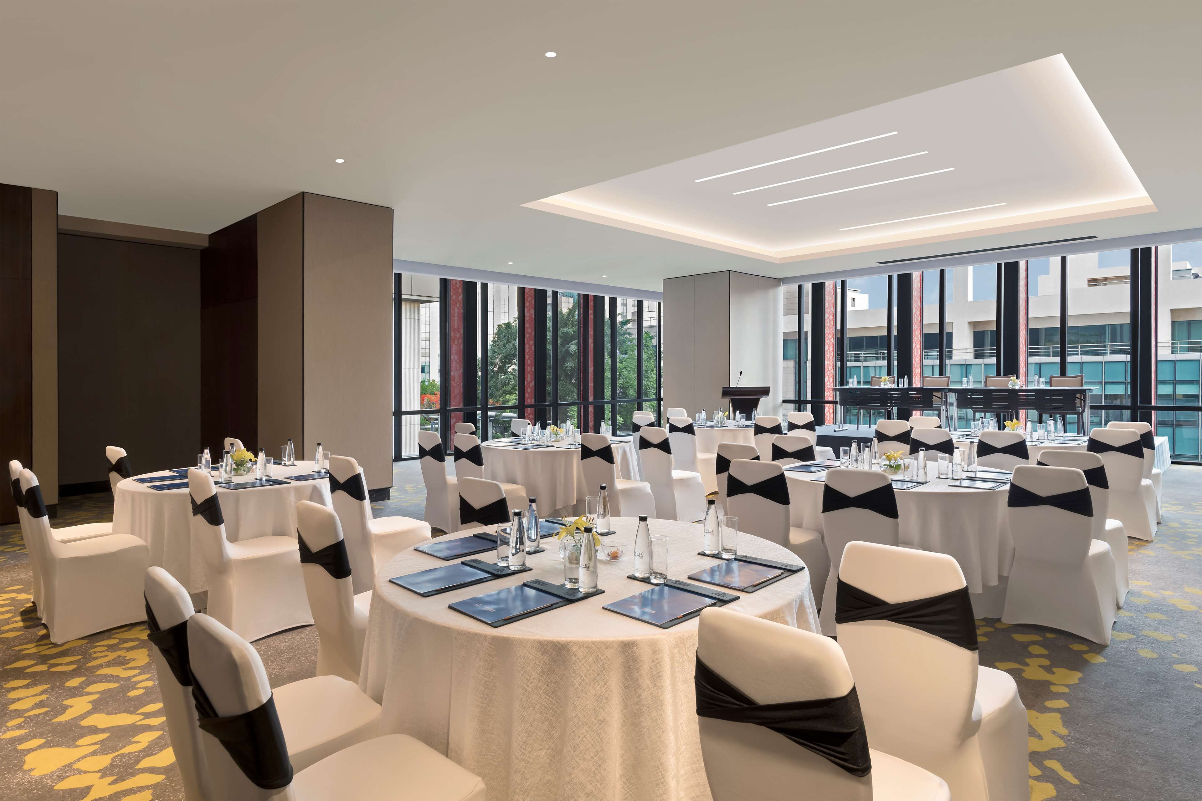 A conference room with round tables, white chairs, and black sashes, equipped with water bottles and place settings.
