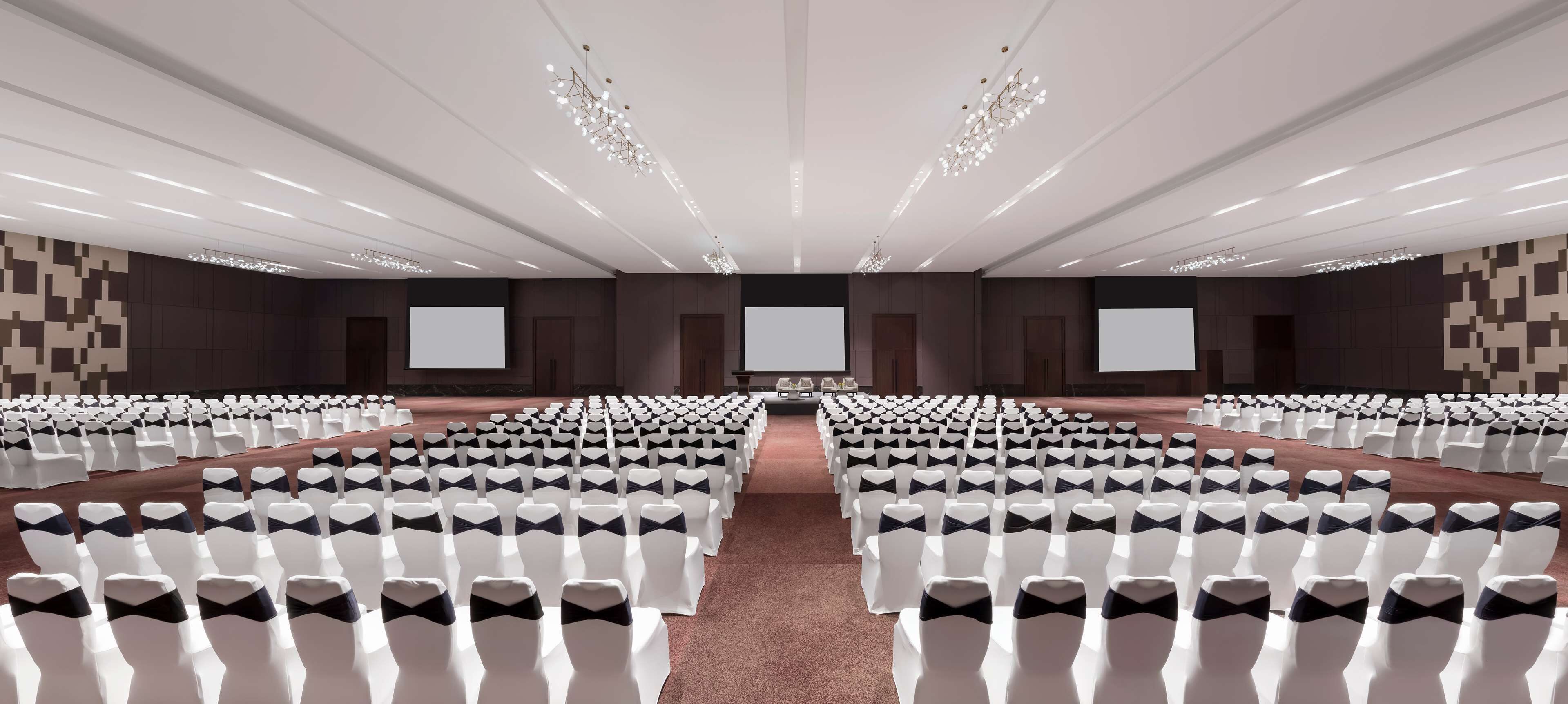 A large conference room with rows of white chairs, black chair covers, and a central stage with a projector screen.