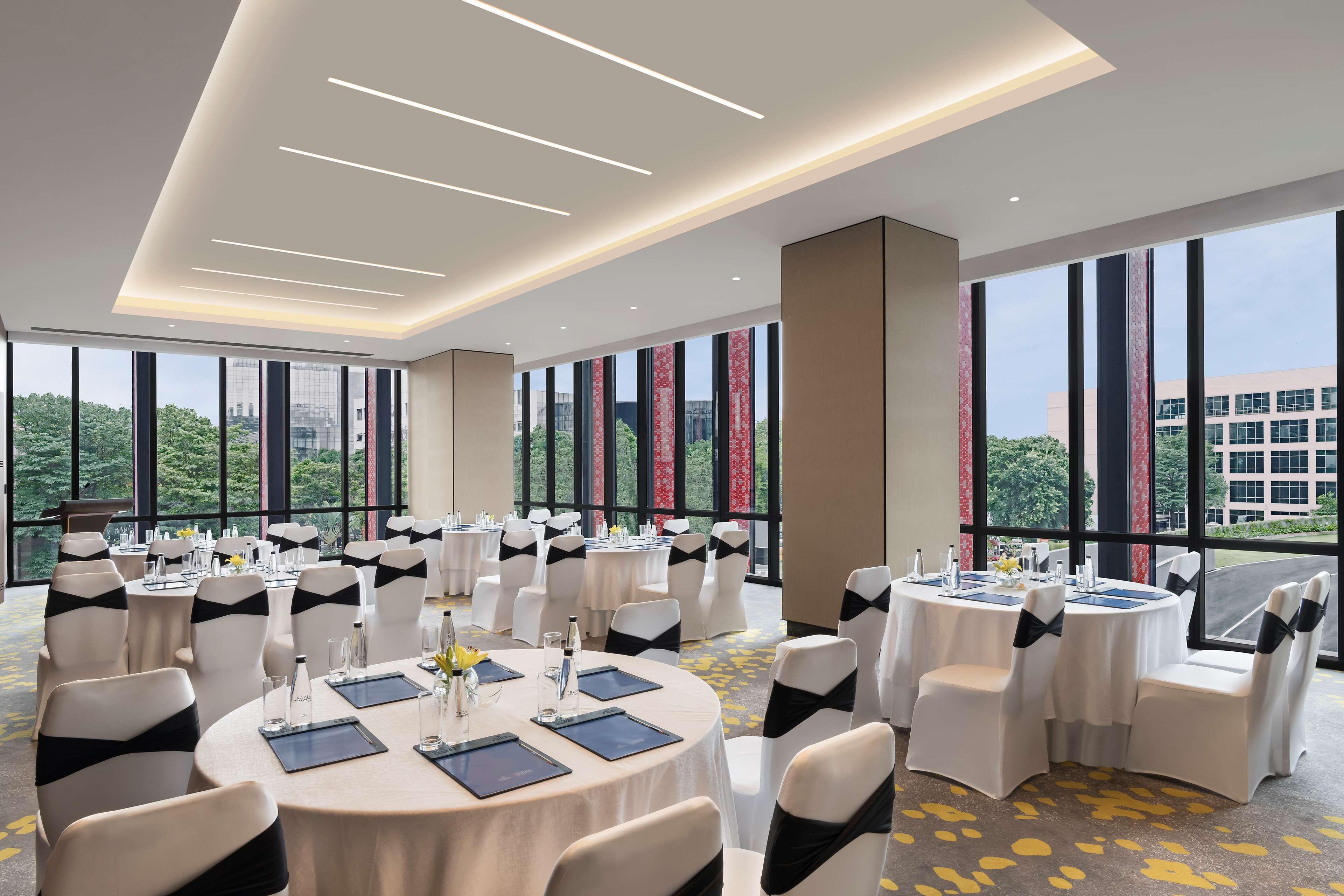 A conference room with multiple round tables, white chairs with black sashes, and large windows offering a city view.