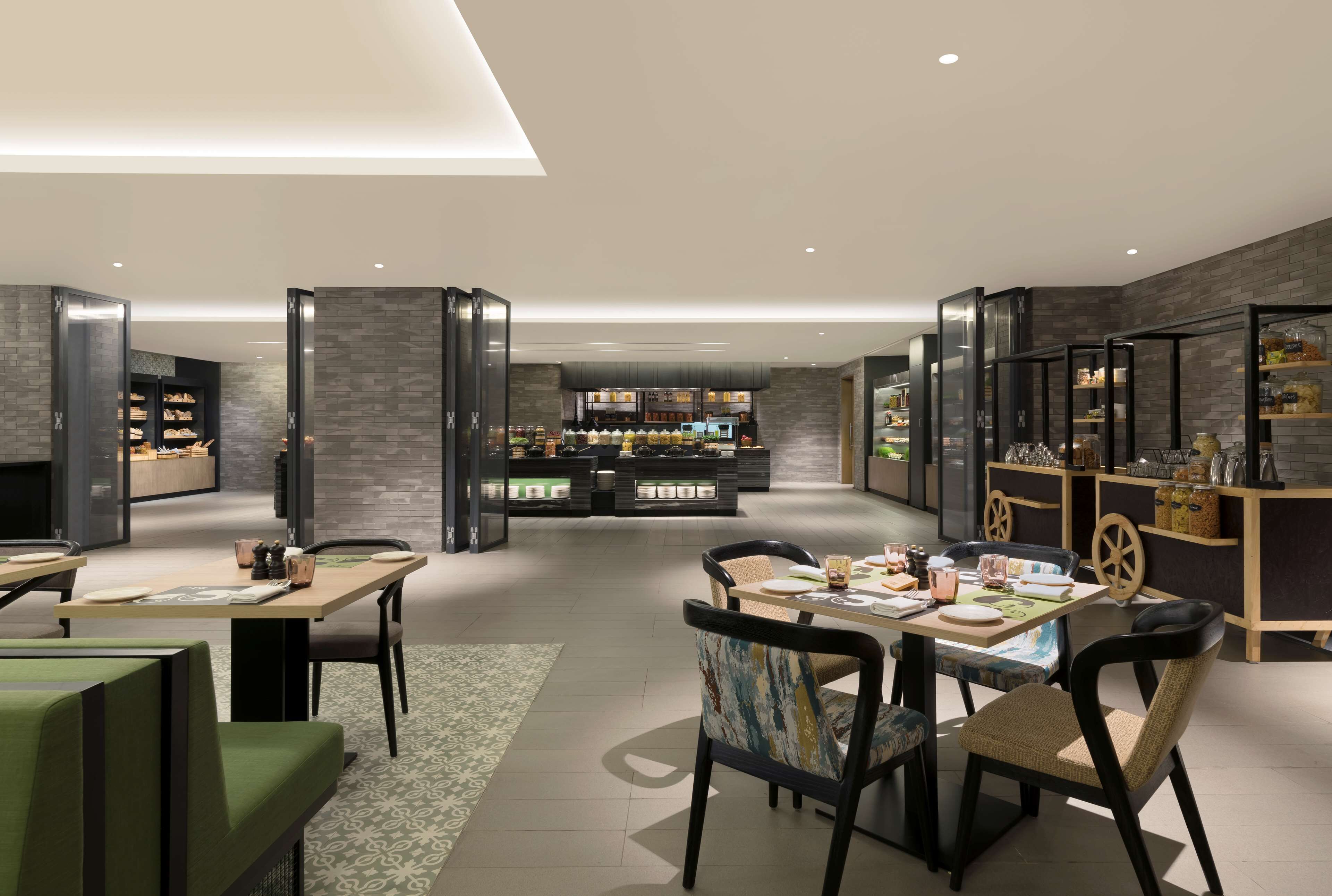 A modern restaurant with a central dining area, a bar, and a kitchen visible in the background.