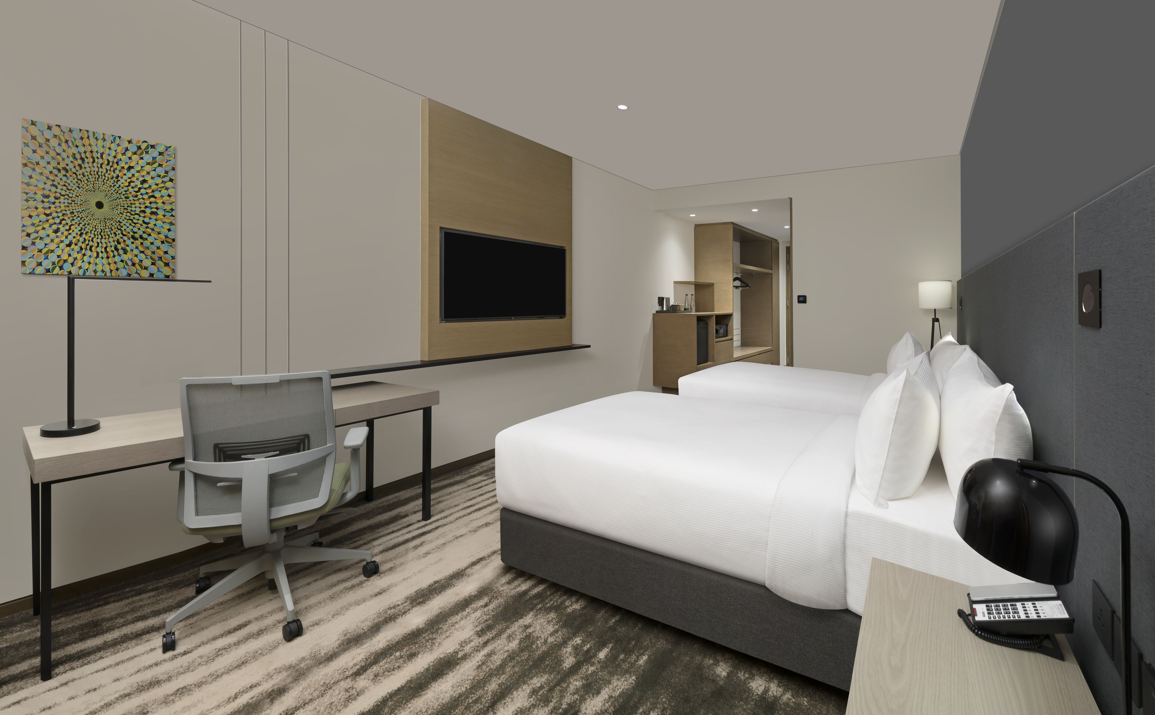 Una habitación de hotel moderna con una cama grande, un escritorio con una silla, un televisor de pantalla plana, una lámpara de escritorio, un teléfono y un espejo.