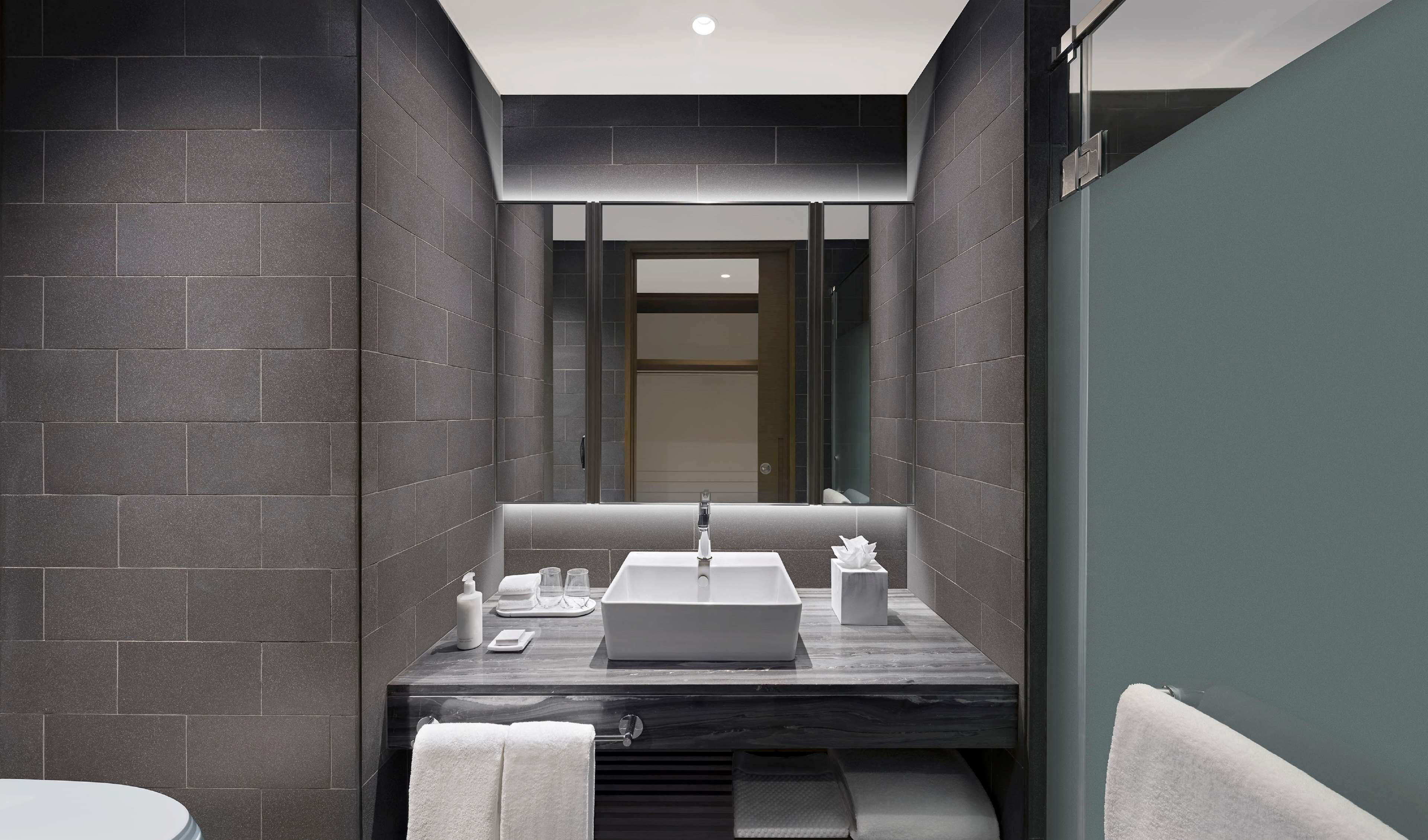 A modern bathroom with dark tiled walls, a marble countertop, a sink, and a mirror.