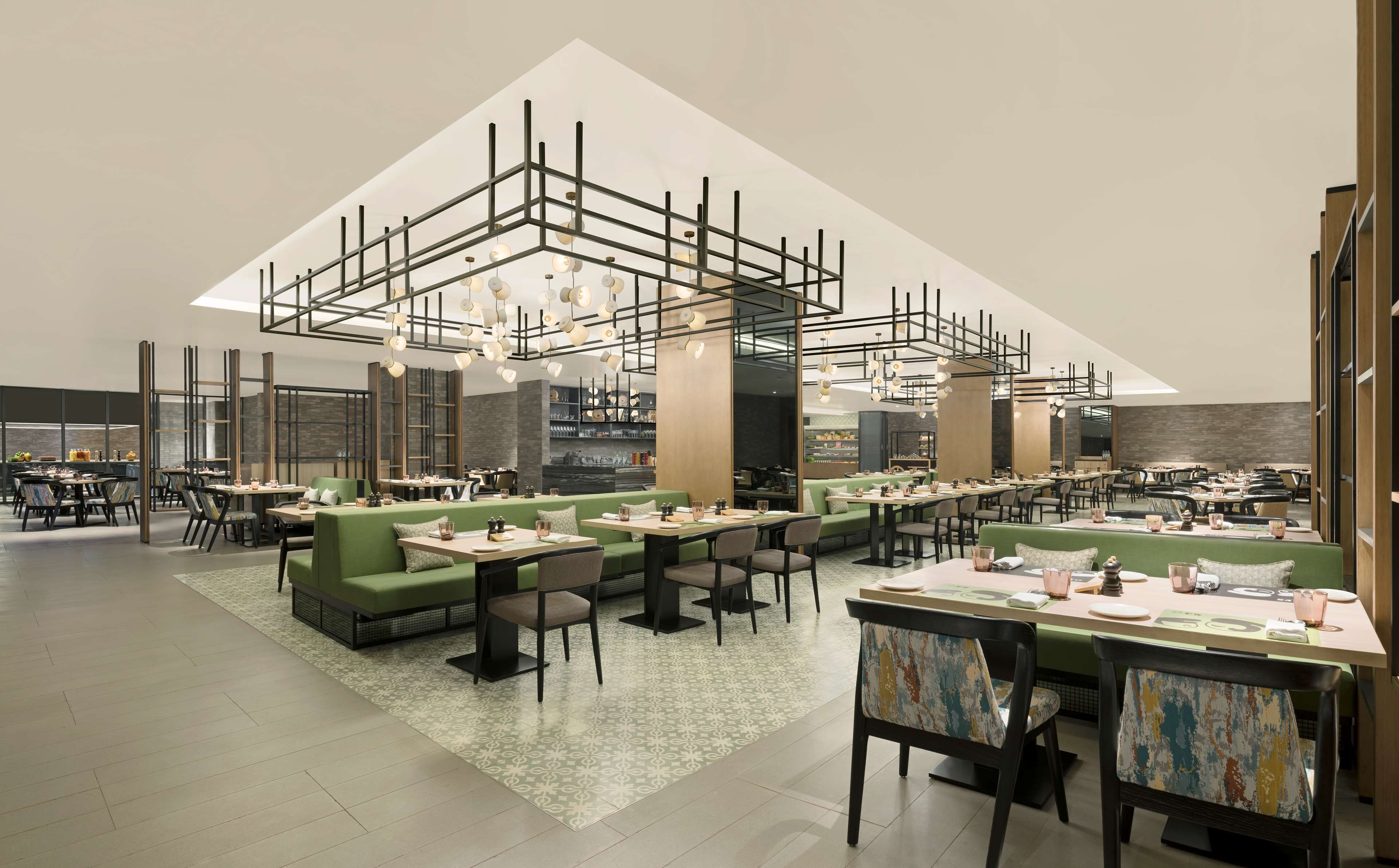Ein modernes Restaurant mit hohen Decken, grünen Sitzbereichen und einer zentralen Bar.