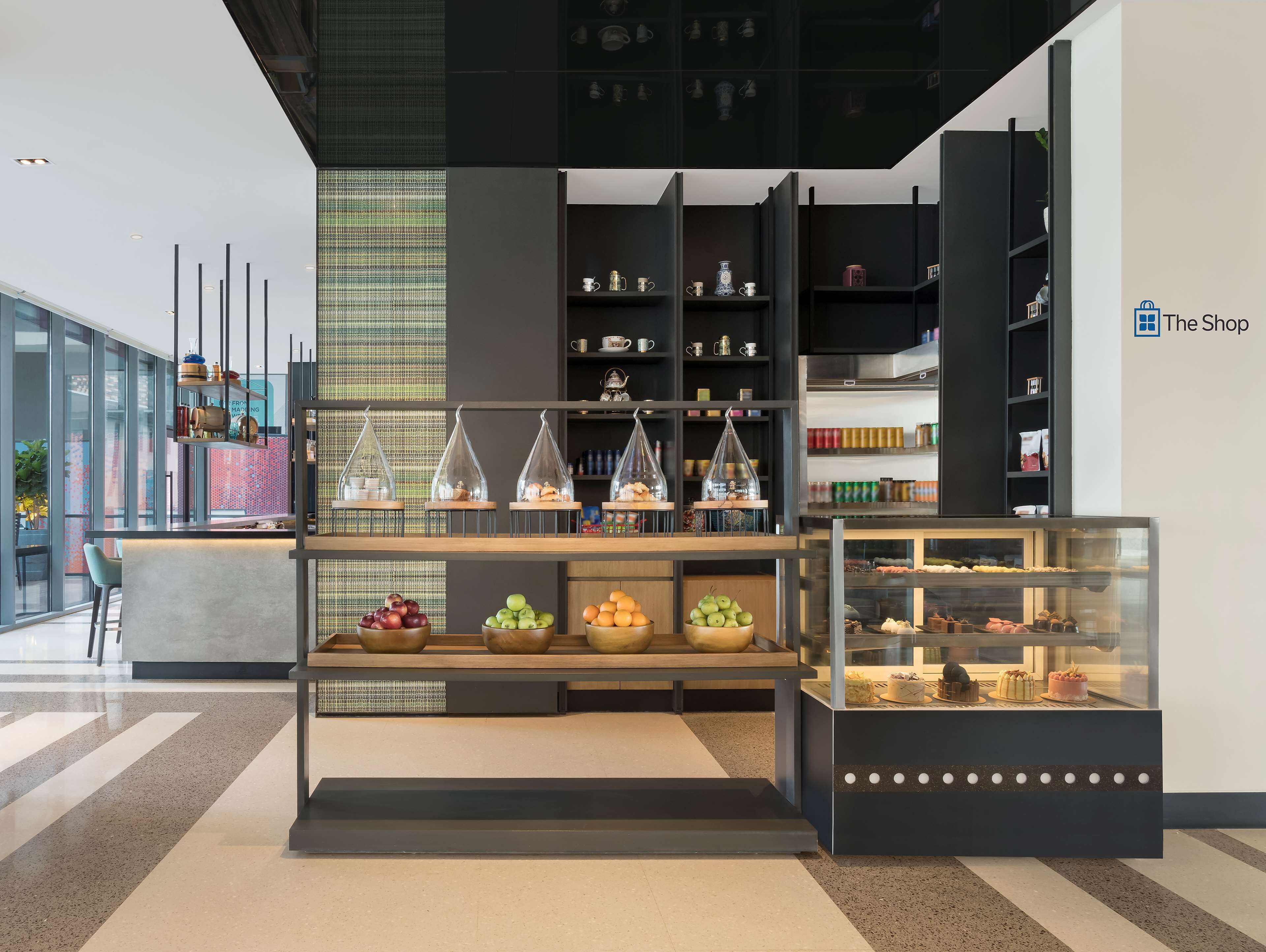 A modern interior with a display counter featuring fruits, a glass case with pastries, and shelves with kitchenware.