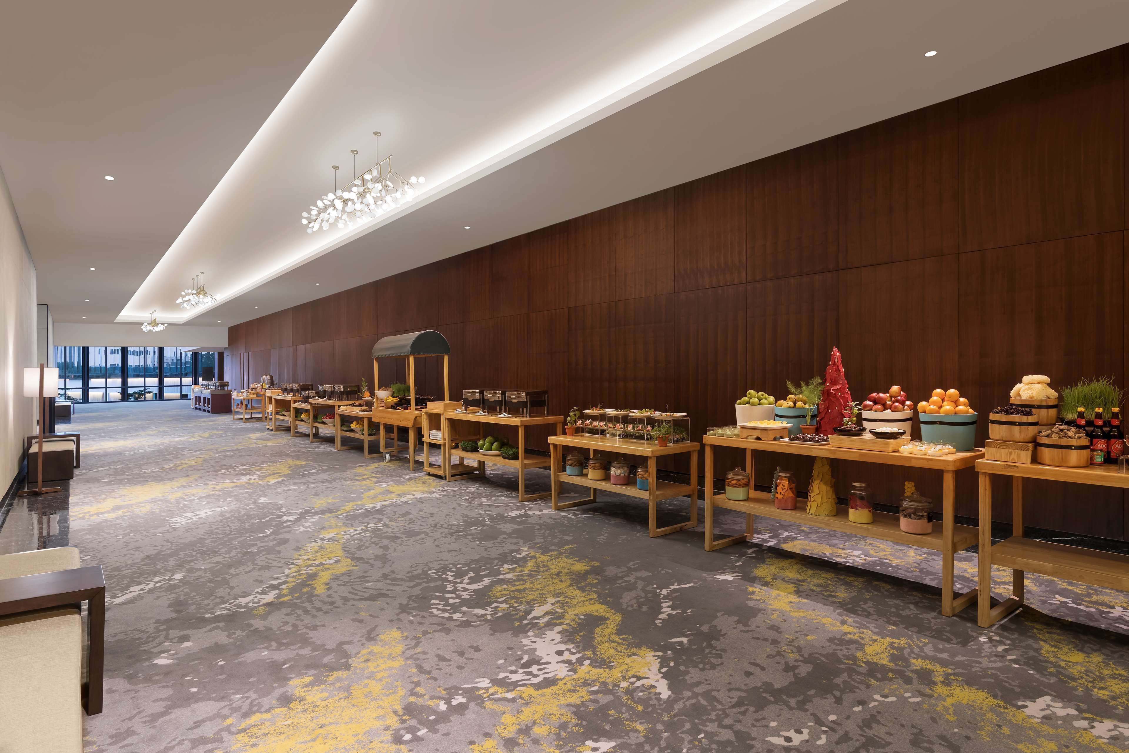 Un hall d’hôtel spacieux, avec des tables en bois où sont exposés divers aliments et plantes.