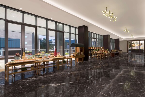 Un vestíbulo amplio con suelo de mármol, ventanas grandes y una larga mesa de buffet con diferentes opciones de comida.