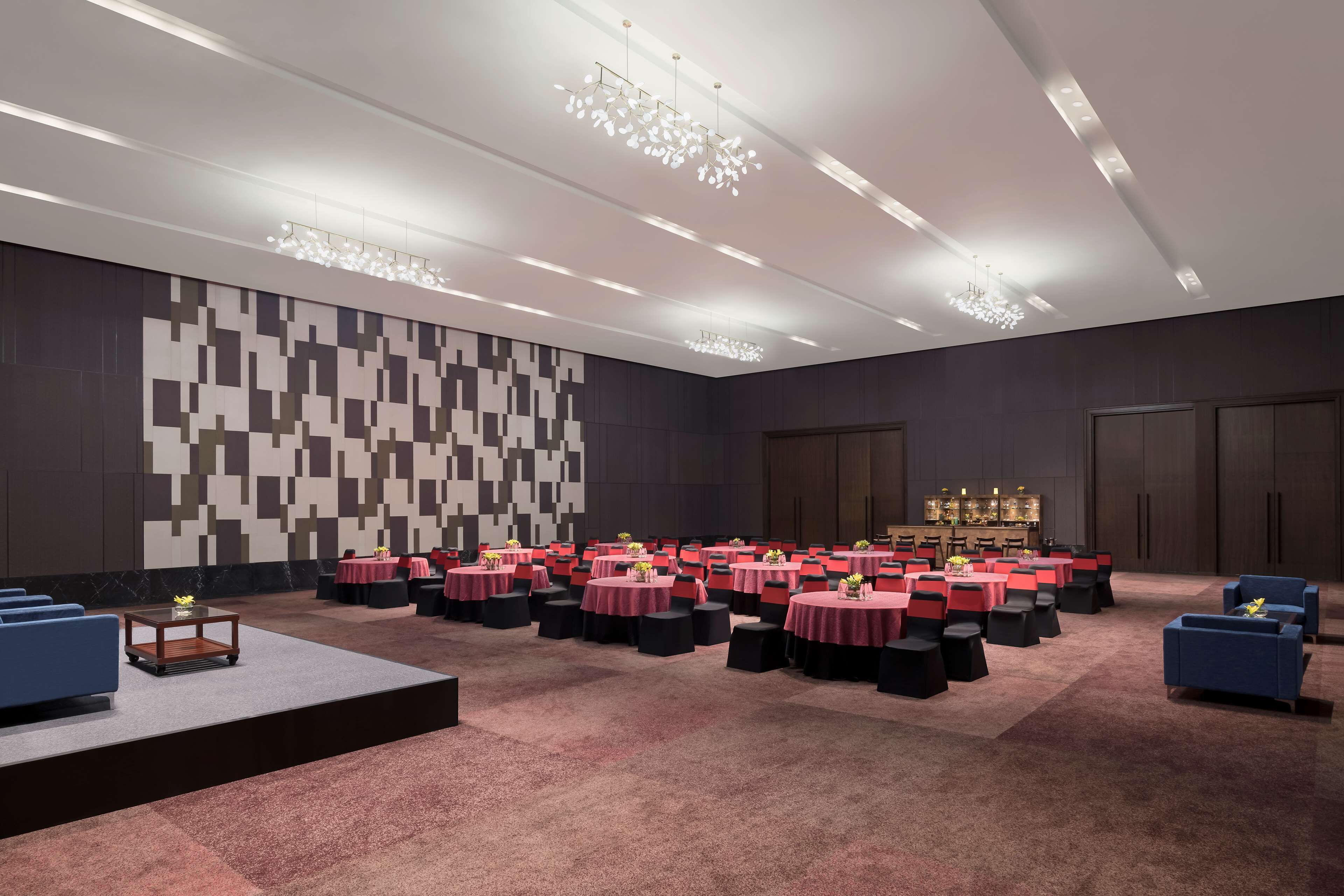 A conference room with round tables, black and red chairs, and a stage.