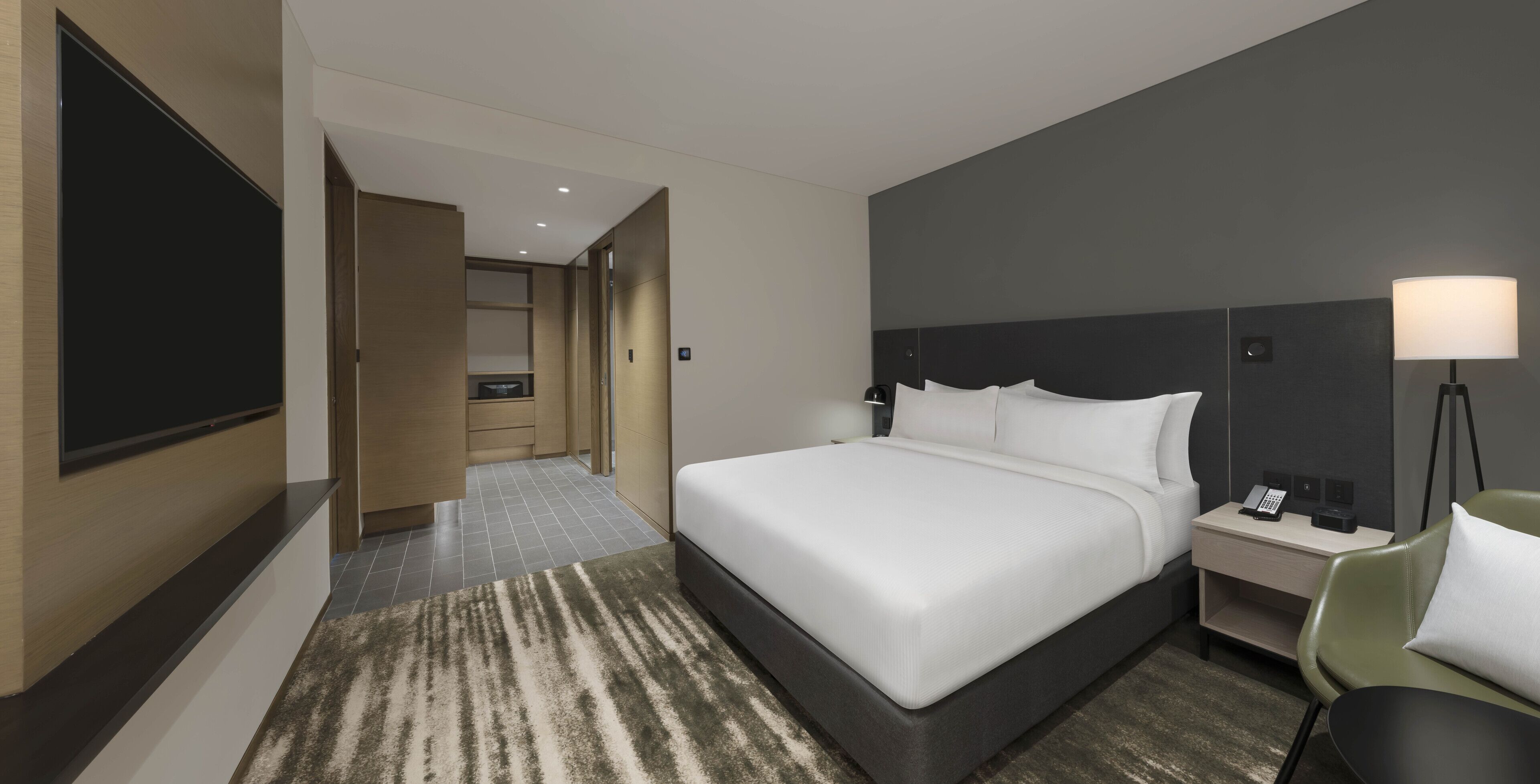 Une chambre d’hôtel avec un grand lit, un bureau avec une lampe, une télévision et une salle de bain visible à travers une porte ouverte.