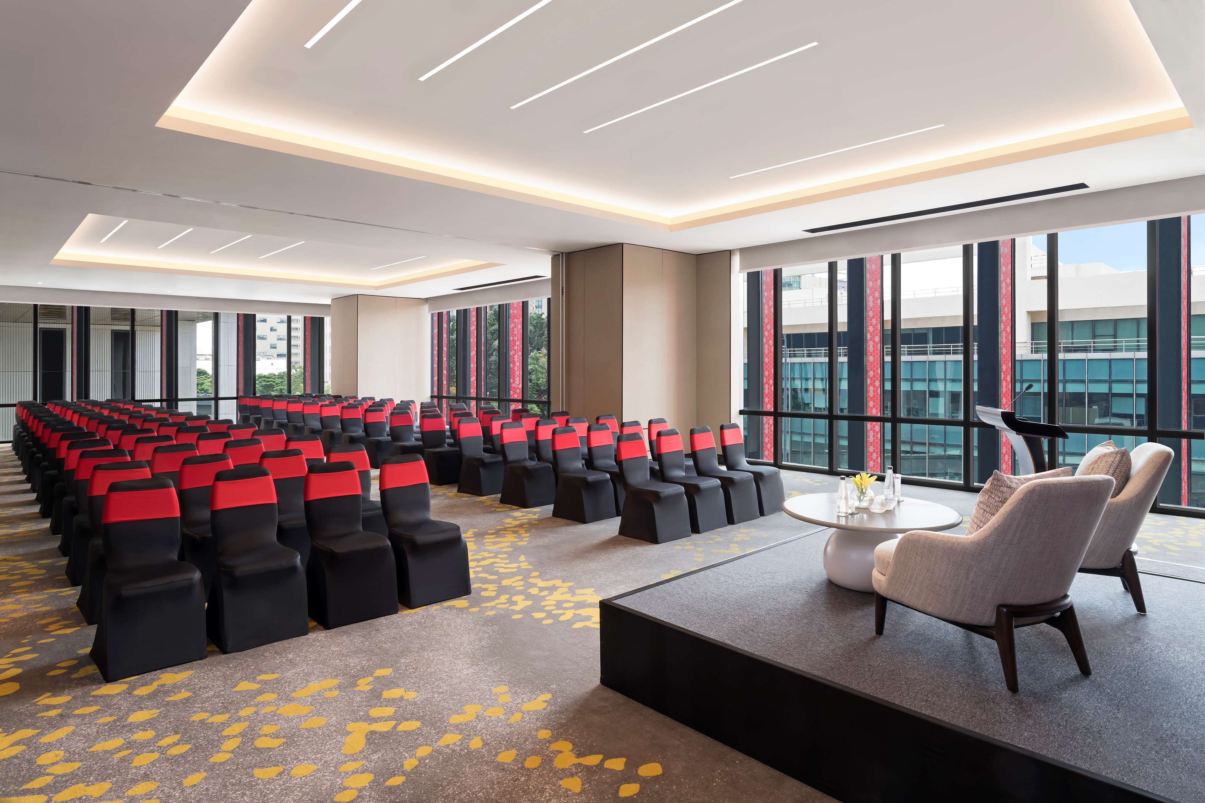 A conference room with rows of chairs, a stage, and a seating area with tables.