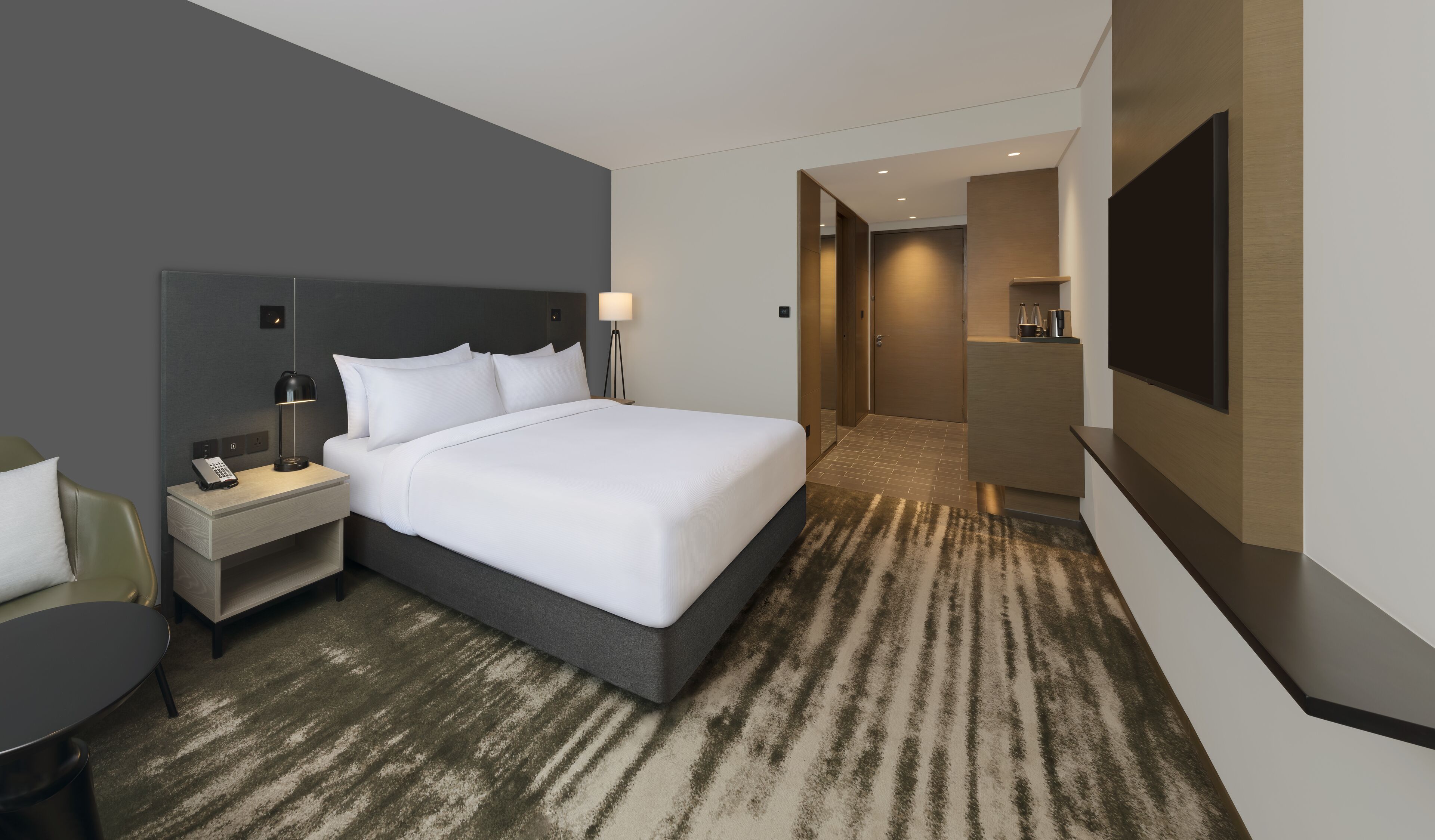 Une chambre d’hôtel moderne dotée d’un grand lit, d’un bureau avec une lampe, d’une chaise, d’une télévision et d’un petit coin cuisine.