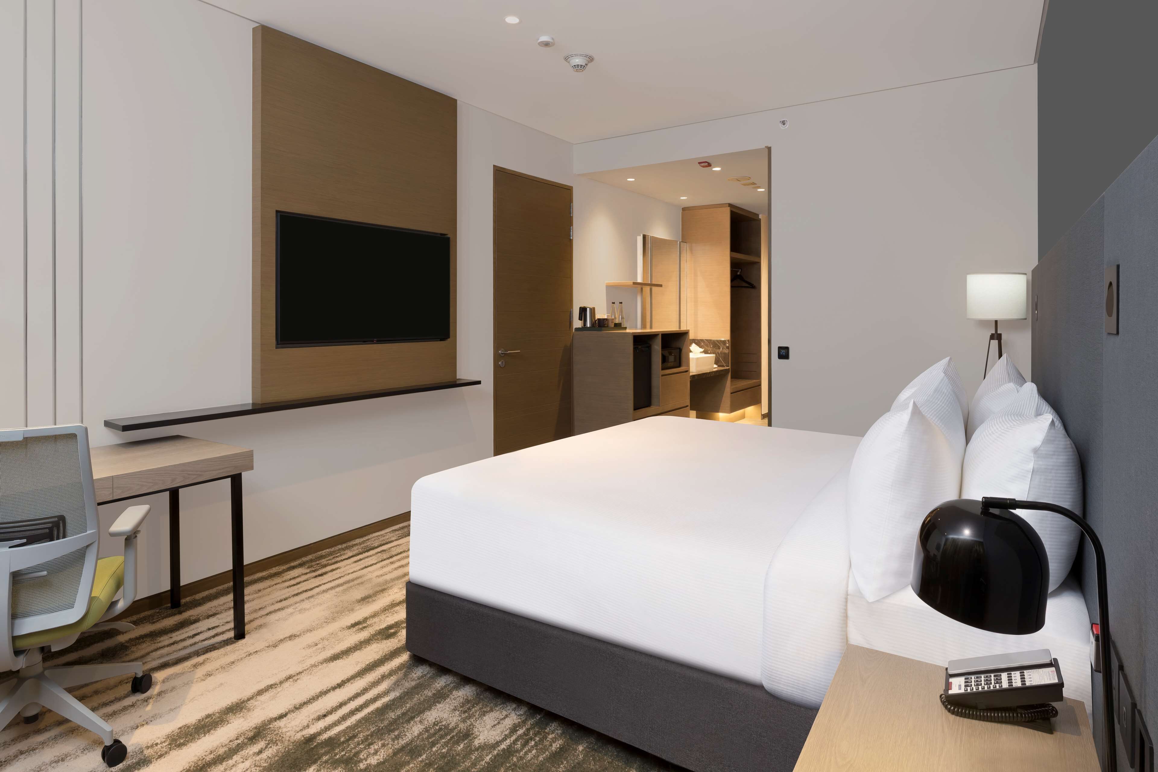 Una habitación de hotel moderna con una cama grande, un escritorio con silla, un televisor montado en la pared, una lámpara de noche y un teléfono.
