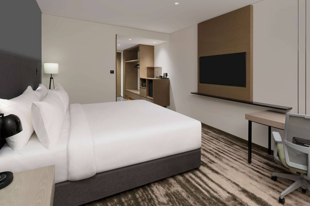 A hotel room with a large bed, a desk, a chair, a TV, and a wardrobe.