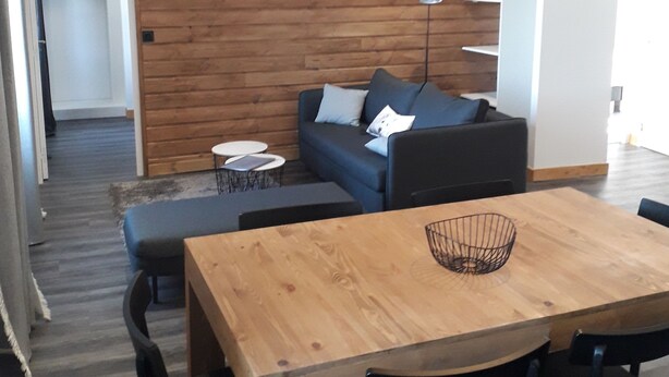 Un salon moderne avec un mur en bois, un canapé bleu, une table à manger en bois avec des chaises et une lampe suspendue.