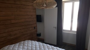 Une chambre à coucher avec une tête de lit en bois, un lit blanc matelassé, un luminaire en fibres tressées, une porte et une fenêtre avec des rideaux.