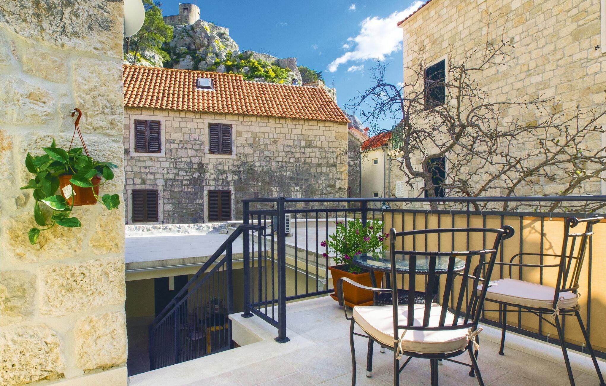 Un balcon avec une table et des chaises, une plante suspendue et une vue sur un bâtiment en pierre avec un toit en tuiles.