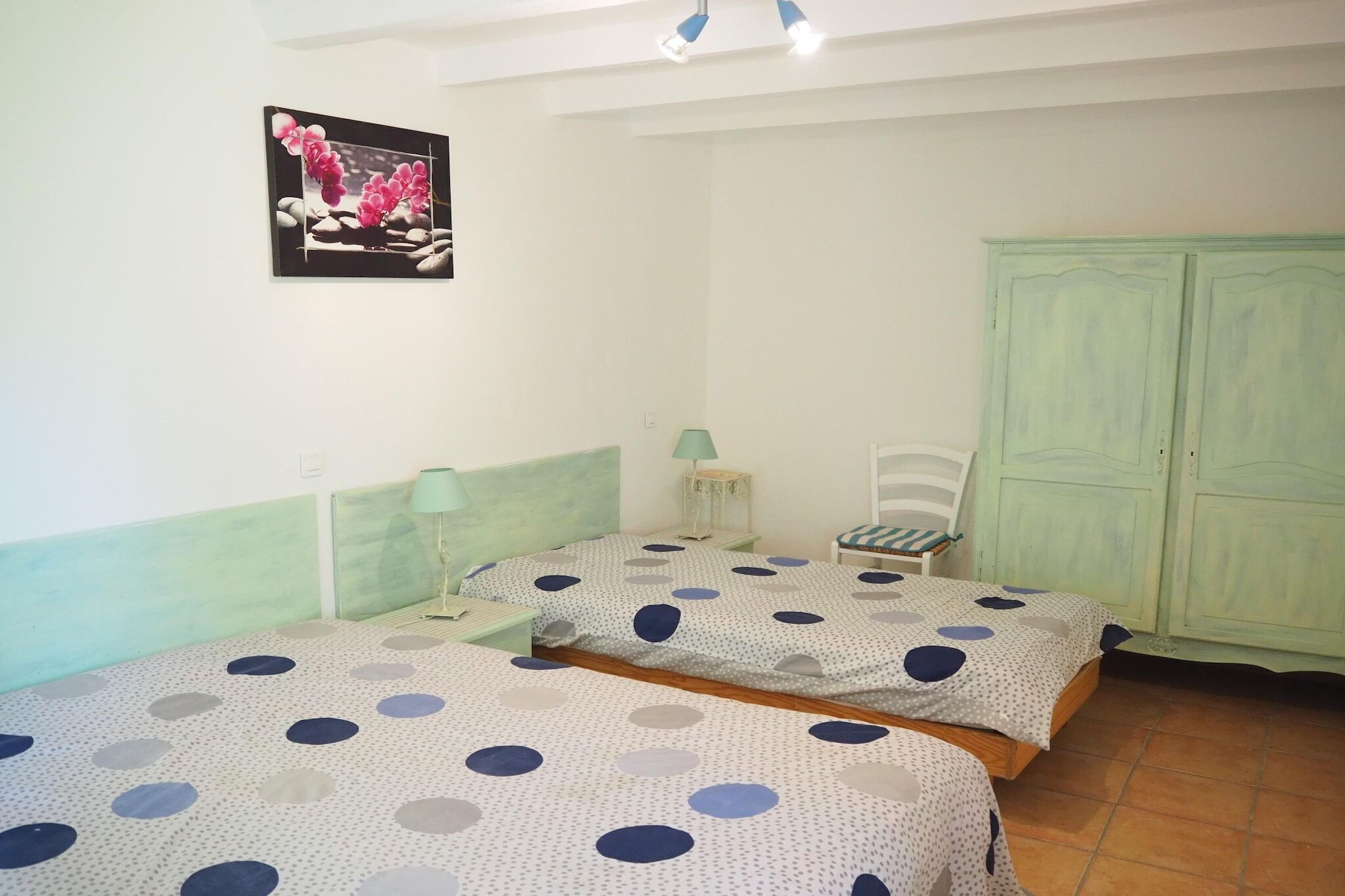 Een kamer met twee bedden, een groene garderobe, een klein tafeltje met een lamp en een lijst met een afbeelding aan de muur.