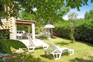 An outdoor seating area with white plastic chairs and tables, a pergola, and a gazebo with an umbrella.
