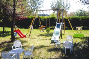 Un parque infantil con columpios, un tobogán y sillas de plástico.