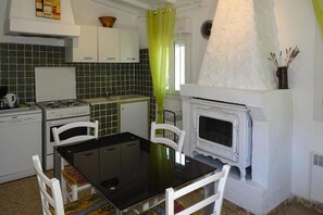 A compact kitchen with a gas stove, white cabinets, a dining table with chairs, and a white fireplace.