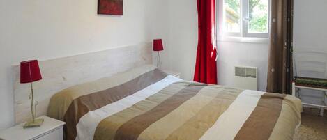 A bedroom with a bed, two bedside lamps, a window with curtains, and a radiator.