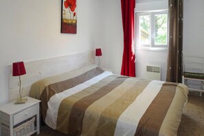 A bedroom with a bed, two bedside lamps, a window with curtains, and a radiator.