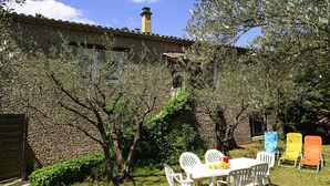 A stone building with a tiled roof, surrounded by olive trees and a small patio with white chairs and a table. - Villa in Provence near Mont Ventoux (Vaison-la-Romaine)