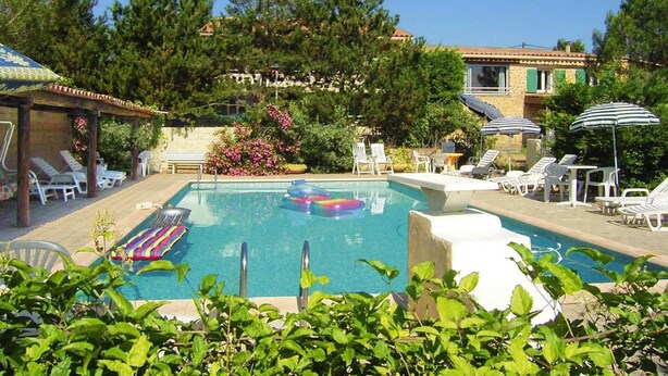 A pool area with lounge chairs, a floating pool toy, and a building with a tiled roof in the background. - Villa in Provence near Mont Ventoux (Vaison-la-Romaine)