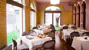 Een restaurant met meerdere eettafels, met een bakstenen muur en rondboogvensters.