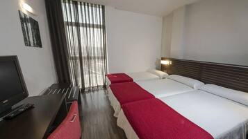 Een hotelkamer met een bureau, twee bedden, een televisie en een raam met gordijnen.