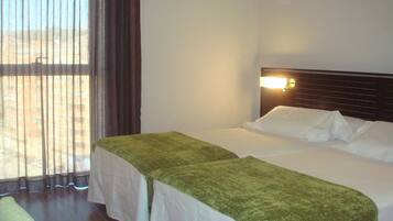 A hotel room with two beds, a window with curtains, and a wall-mounted light fixture.