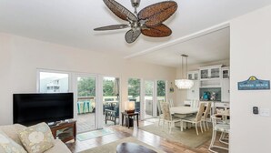 A spacious living room with a large TV, a ceiling fan, and a dining area with chairs and a table.