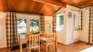 Un coin repas chaleureux avec une table et des chaises en bois, des rideaux à carreaux et une horloge au mur.