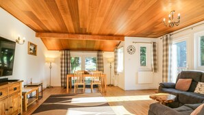 Un salon chaleureux avec un plafond en bois, un coin repas avec une table et des chaises, un canapé et un téléviseur.