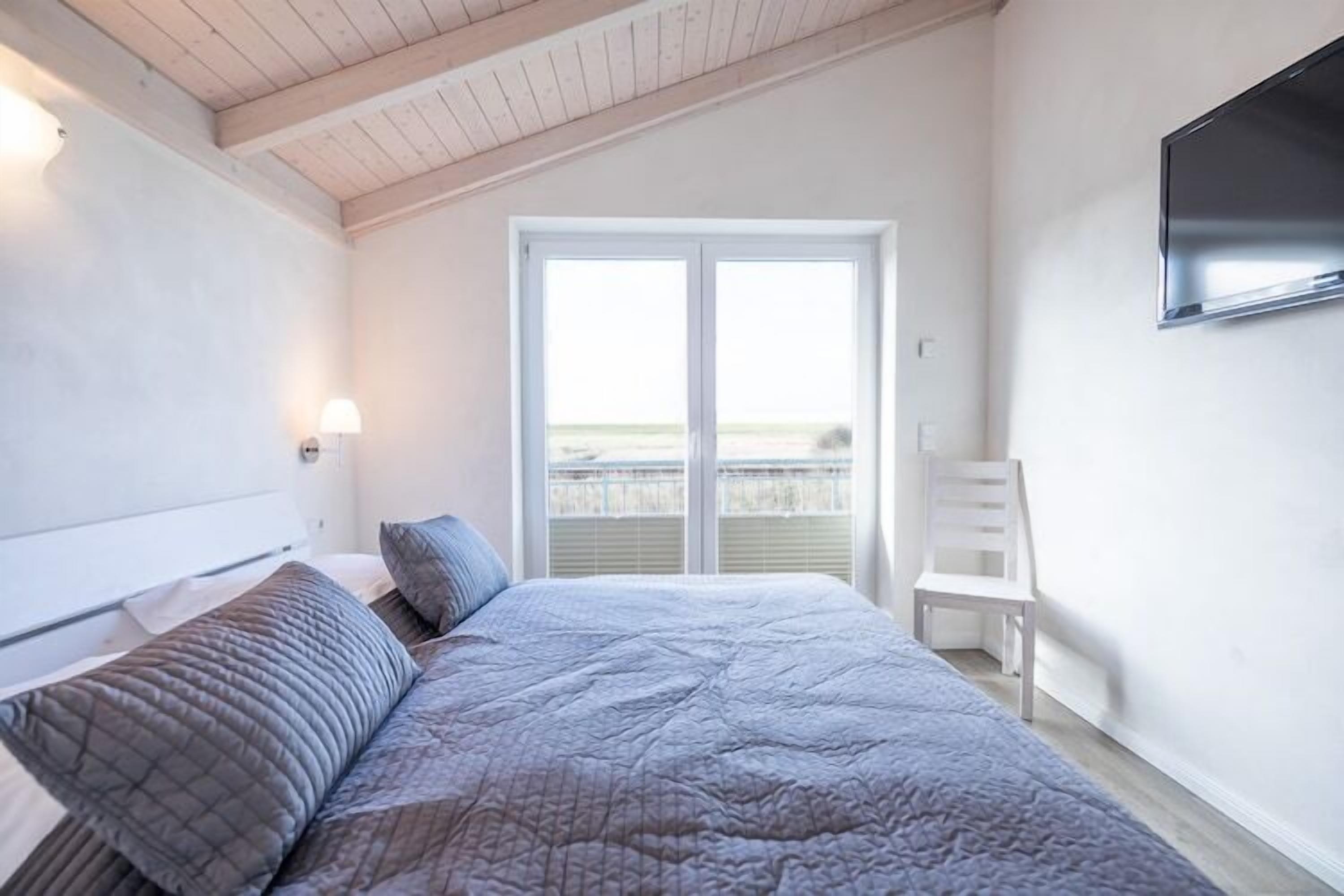 Une chambre avec un lit, une chaise, une télévision et un balcon offrant une vue.