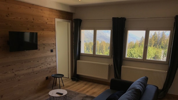 Una sala de estar moderna con una pared de madera, un sofá negro, una mesa de centro redonda y un televisor montado en la pared.