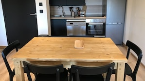 Una cocina moderna con una mesa de comedor de madera, sillas negras y electrodomésticos de acero inoxidable, incluyendo lavavajillas, horno y refrigerador.