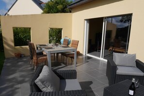 Une terrasse extérieure avec une table à manger, des meubles en osier et une bouteille de vin.