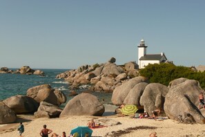 Une plage avec de gros rochers, un phare et des gens qui prennent un bain de soleil.