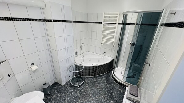 A modern bathroom with white tiles, a black and white tiled shower area, a glass-enclosed shower, a white bathtub, and a toilet.