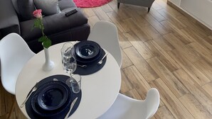 A modern living room with a sofa, a dining table set for two, a chandelier, and a view of the outdoors through large windows. - The Apartment is in a calm, quiet location at the Lake Balaton! (Keszthely)