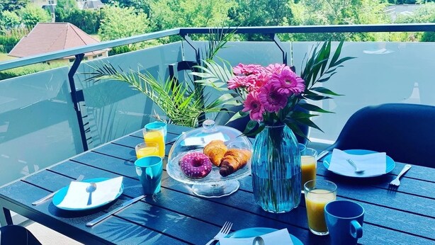 A table set outdoors with breakfast items, a vase of flowers, and a scenic view in the background. - The Apartment is in a calm, quiet location at the Lake Balaton! (Keszthely)